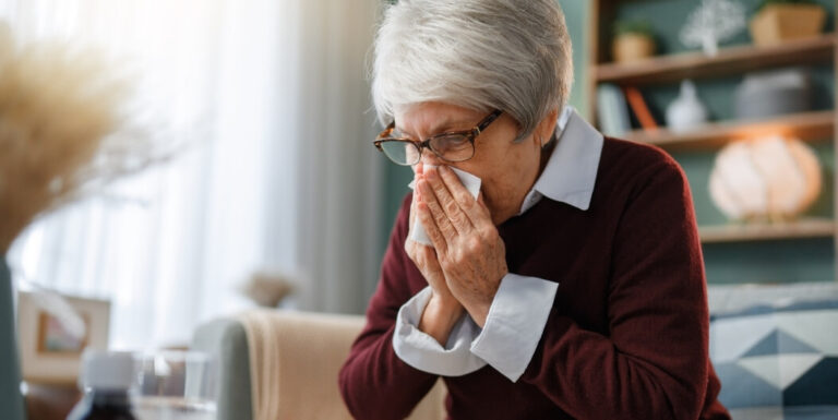 Elderly Woman Blowing Her Nose with Allergy Medication Nearby at Assisted Living Facility
