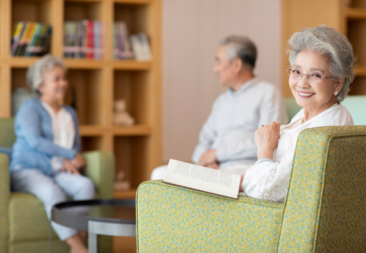 Smiling Elderly Woman Reading Book at Memory Care Facility Smiling Elderly Woman Reading Book at Memory Care Facility